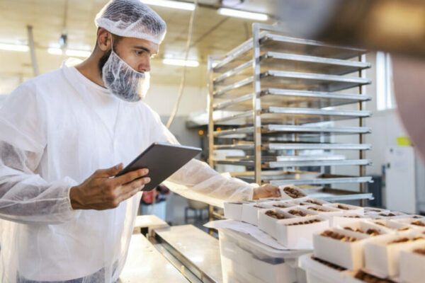 A food inspector in a sterile white uniform is holding the tablet and looking at collected cookies. Food check is important if we want quality and healthy food.
